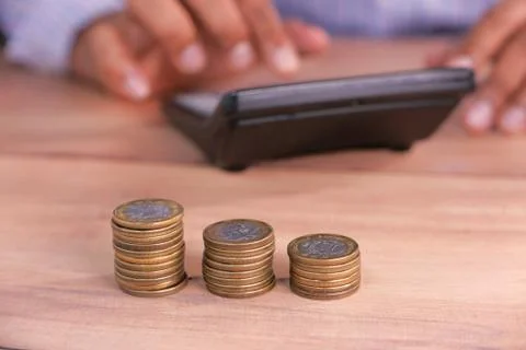 Stack of coins on table and man using calculator on background Stock Photos