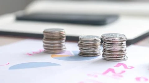 A stack of coins on a table next to a graph Stock Photos