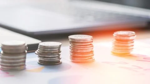 A stack of coins on a table next to a laptop Stock Photos