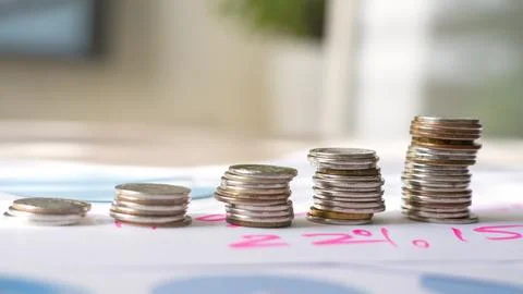 A stack of coins on a table with a pink background Stock Photos