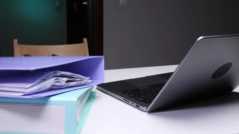 Stack of colorful binders and files with a laptop on a white desk, representing Stock Footage 324764238