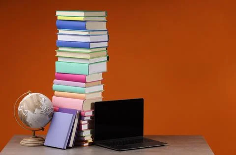 Stack of colorful books, globe and laptop on wooden table against orange ba.. Foto stock