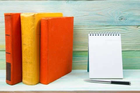 Stack of colorful books, notebook with blank sheet paper and pen on wooden table Stock Photos