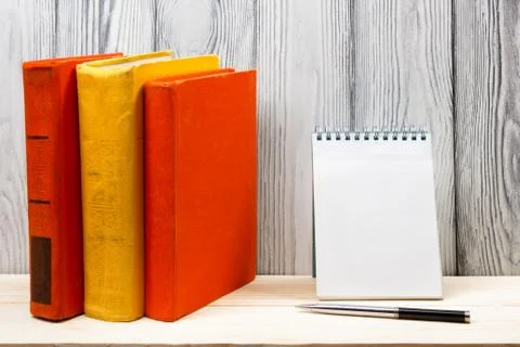 Stack of colorful books, notebook with blank sheet paper and pen on wooden table Stock Photos