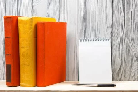 Stack of colorful books, notebook with blank sheet paper and pen on wooden table Stock Photos