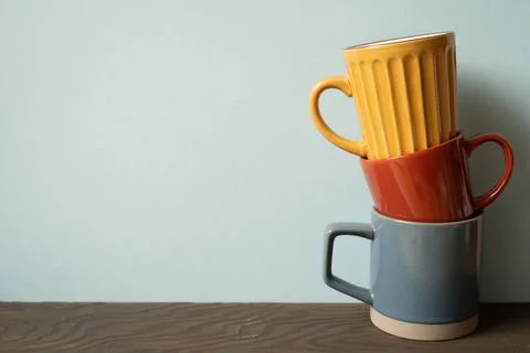 Stack of colorful ceramic mug cups on wooden table. blue wall background S... Stock Photos