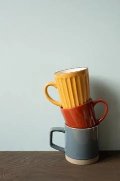 Stack of colorful ceramic mug cups on wooden table. blue wall background S... Stock Photos