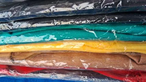 Stack of colorful cotton shirts wrapped in clear protective plastic packaging Stock Photos