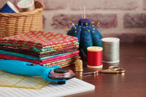Stack of colorful fabrics on table surrounded by sewing accessories on bric.. Fotos de archivo
