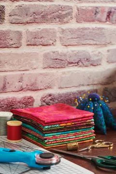 Stack of colorful fabrics on table surrounded by sewing accessories on bric.. 스톡 사진