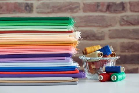 Stack of colorful monochromatic fabrics and spools of thread on brick wall .. Fotos de archivo