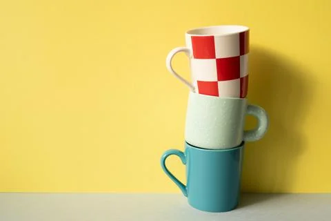 Stack of colorful mug cups on gray table. yellow wall background Stock Photos