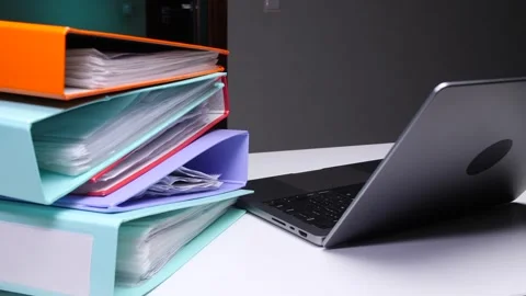 Stack of colorful office binders and a modern laptop on a white desk Stock Footage 324764274
