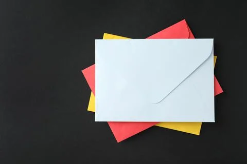 Stack of colorful paper envelopes on black background, top view Foto stock