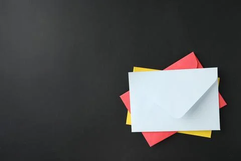 Stack of colorful paper envelopes on black background, top view. Space for te 写真素材