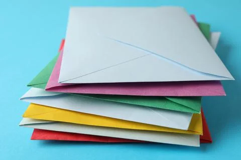 Stack of colorful paper envelopes on light blue background, closeup Foto stock