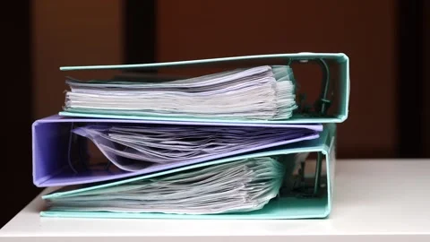 Stack of colorful ring binders overflowing with various business documents Stock Footage 347237415