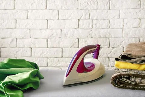 Stack of colour clothes, electric iron and wrinkled shirt on the board Stock Photos