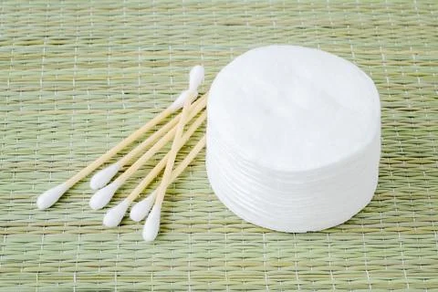 Stack of cotton pads and heap of wood stick cotton buds on a rough wicker mat Stock Photos
