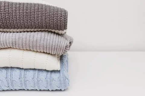 Stack of cozy comfortable homely knitted sweaters in pastel colors, cosy home Stock Photos