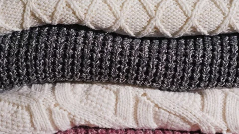 Stack of cozy knitted sweaters in neutral colors for winter warmth and comfor Stock Footage 335018797