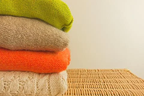 Stack of cozy knitted sweaters on wicker basket Stock Photos