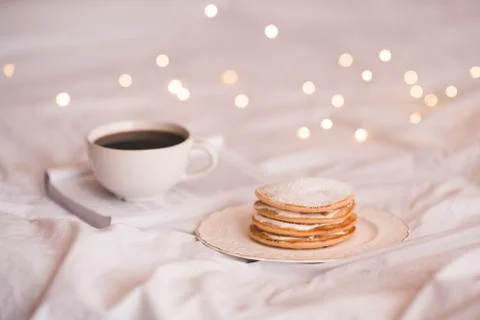 Stack of creamy pancakes with open book and fresh coffee over glowing lights  Stock Photos