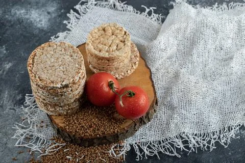Stack of crispbread, tomatoes and raw buckwheat on wooden piece Foto stock
