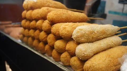Stack of crispy corn dogs in blurred warm market stall display Stock Photos