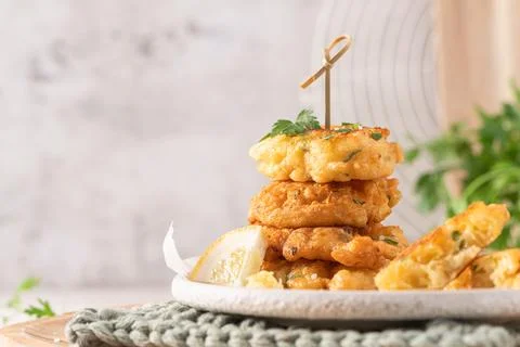 Stack of crispy golden cod fritters on a plate with fresh lemon and parsley.. Stock Photos