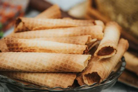 Stack of crispy wafer rolls arranged in a glass bowl on a textured surface .. Stock Photos