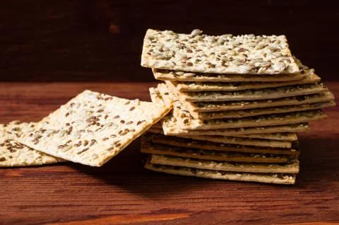 Stack of crispy wheat cakes with sesame seeds, flax and sunflower on a red wo Stock Photos