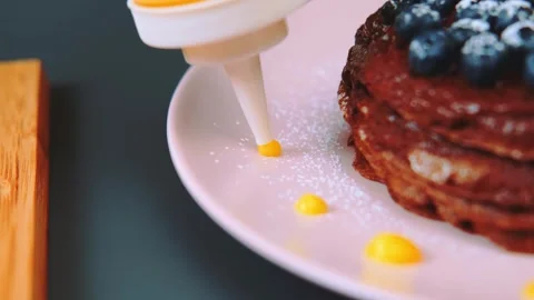 Stack of dark brown pancakes topped with blueberries and orange sauce in kitchen Stock Footage 342863203