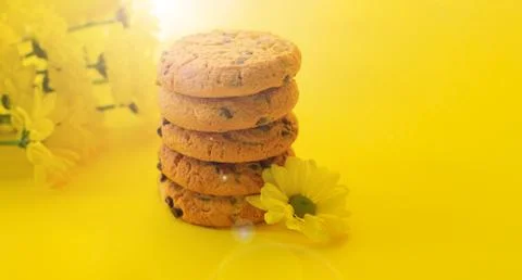 Stack of delicious chocolate chip cookies next to flowers on yellow backgroun Stock Photos