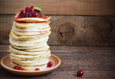 Stack of delicious pancakes with cranberries on plate and napkin wooden backg Stock Photos