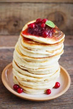 Stack of delicious pancakes with cranberries on plate and napkin wooden backg Stock Photos