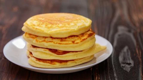 Stack of delicious pancakes in white plate on brown wooden background. It i.. Stock Photos