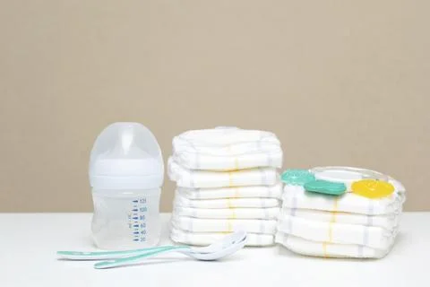 Stack of diapers with bottle of milk and spoons on table. baby's stuff with.. Stock Photos