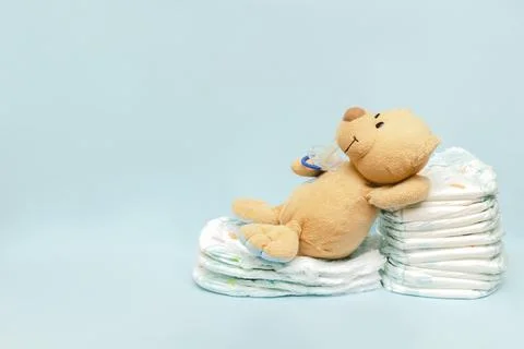 Stack of diapers with cute teddy bear toy pacifier lying on table. set for .. Stock Photos