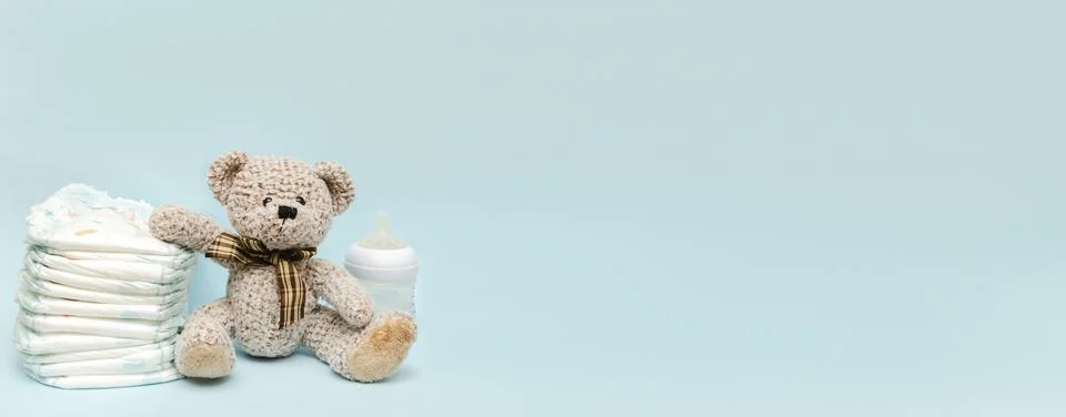 Stack of diapers with cute teddy bear toy, bottle of milk on table. set for i Stock-Fotos