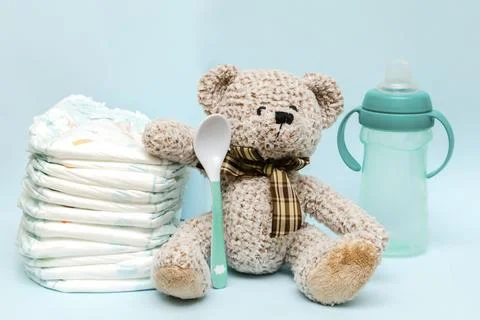 Stack of diapers with cute teddy bear toy, bottle of milk on table. set for.. Stock Photos