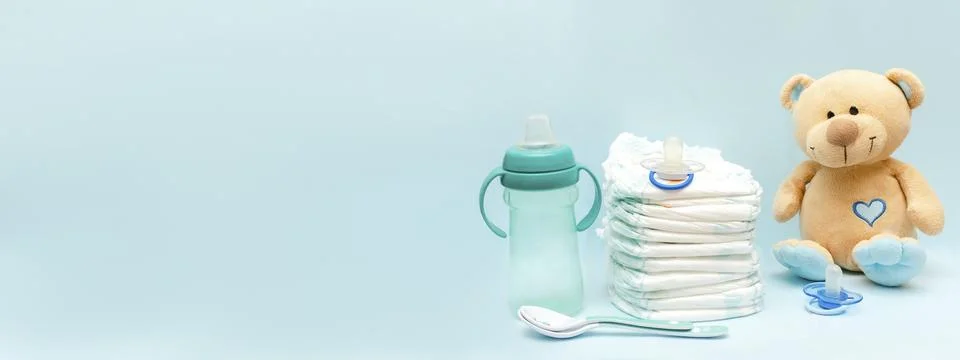 Stack of diapers with cute teddy bear toy, bottle milk, pacifier on table. .. Stock Photos