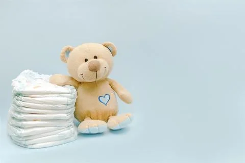 Stack of diapers with cute teddy bear toy on table. set for infant newborn bo Stock Photos