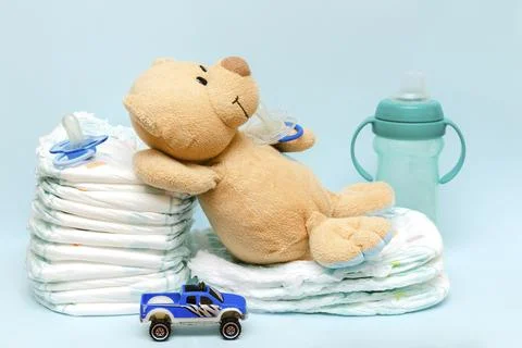 Stack of diapers with cute teddy bear car toy pacifier bottle lying on table. Stock Photos