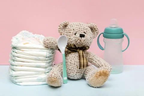 Stack of diapers with cute teddy bear toy, bottle of milk on table. set for i Stock Photos