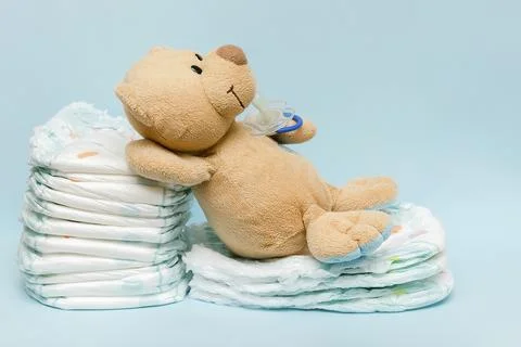 Stack of diapers with cute teddy bear,toy pacifier bottle lying on table. set Stock Photos