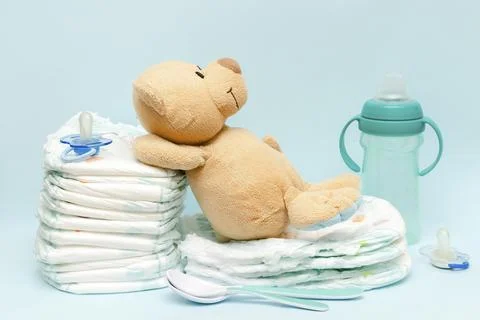 Stack of diapers with cute teddy bear,toy pacifier bottle lying on table. s.. Stock Photos