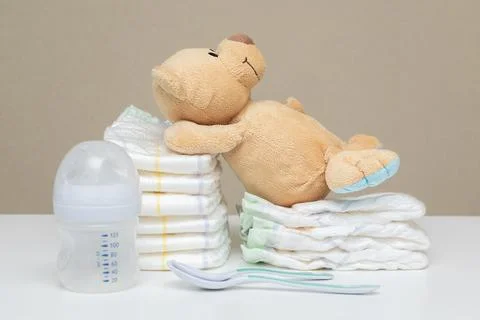 Stack of diapers with teddy bear toy lying on white table, bottle for milk .. Stock Photos