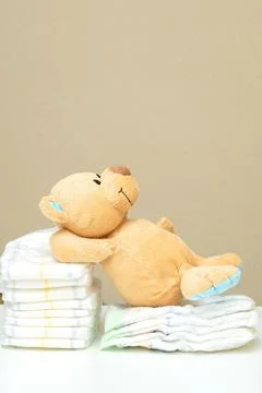 Stack of diapers with teddy bear toy lying on white table. set for children.. Stock Photos