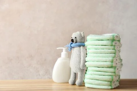 Stack of diapers, toy bear and cream on table against color background, space Stockfoto's